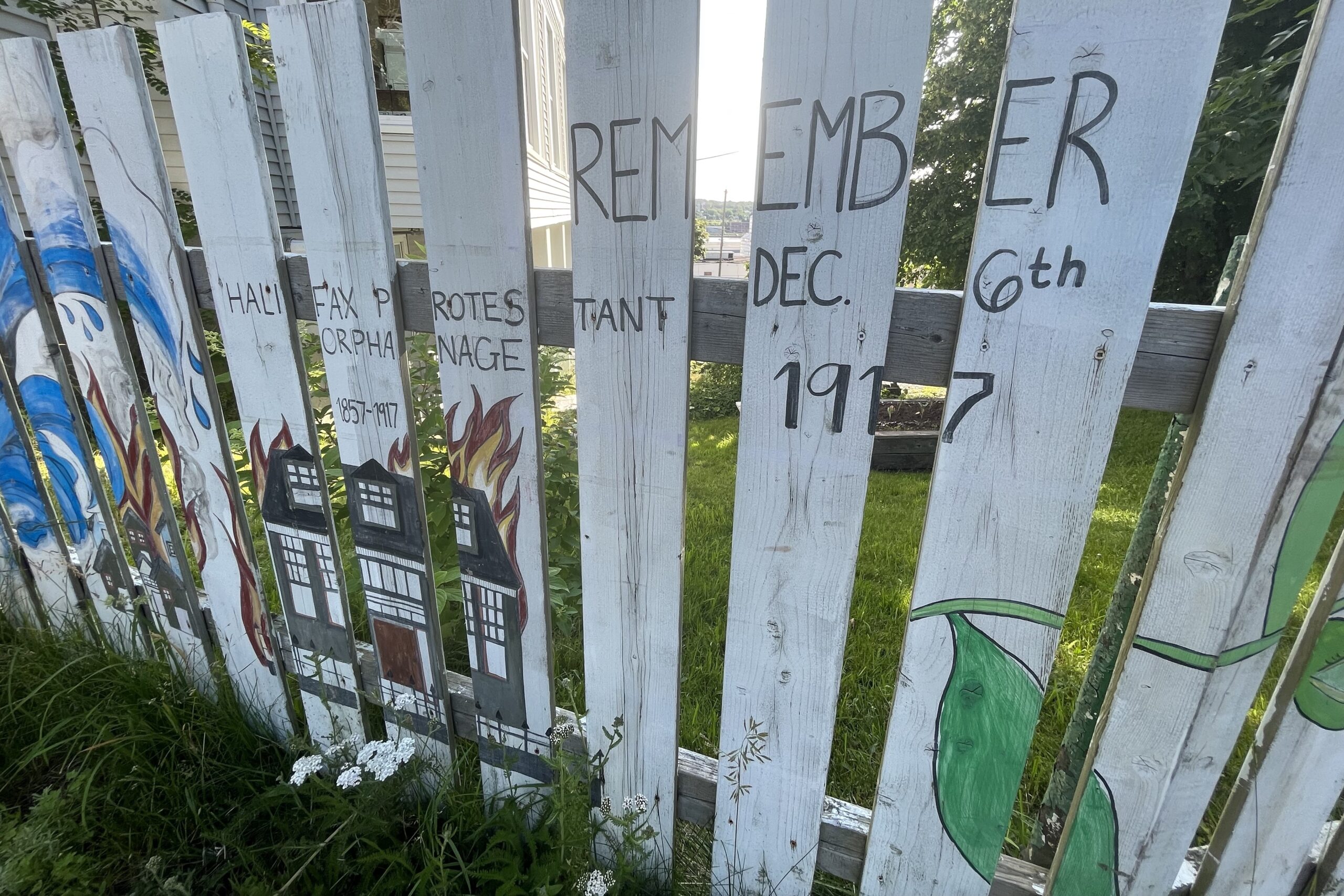 白色的尖桩篱笆上画着一座燃烧的建筑物，上面写着“记住，1917年12月6日，哈利法克斯新教孤儿院1857年至1917年。”