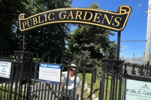 一名妇女把“公园关闭”的牌子固定在大门上。在大门上方是一个更永久的标志，“公共花园”。