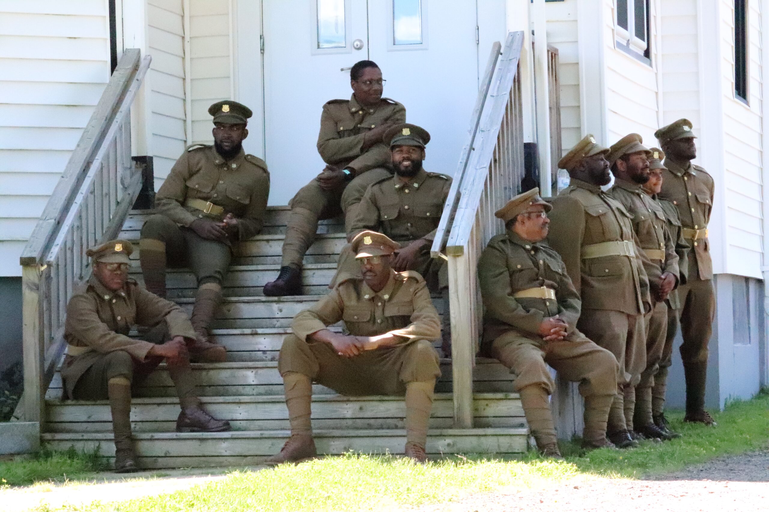 A group of men dressed in early 20th century military uniforms sit on the steps of a historic church.