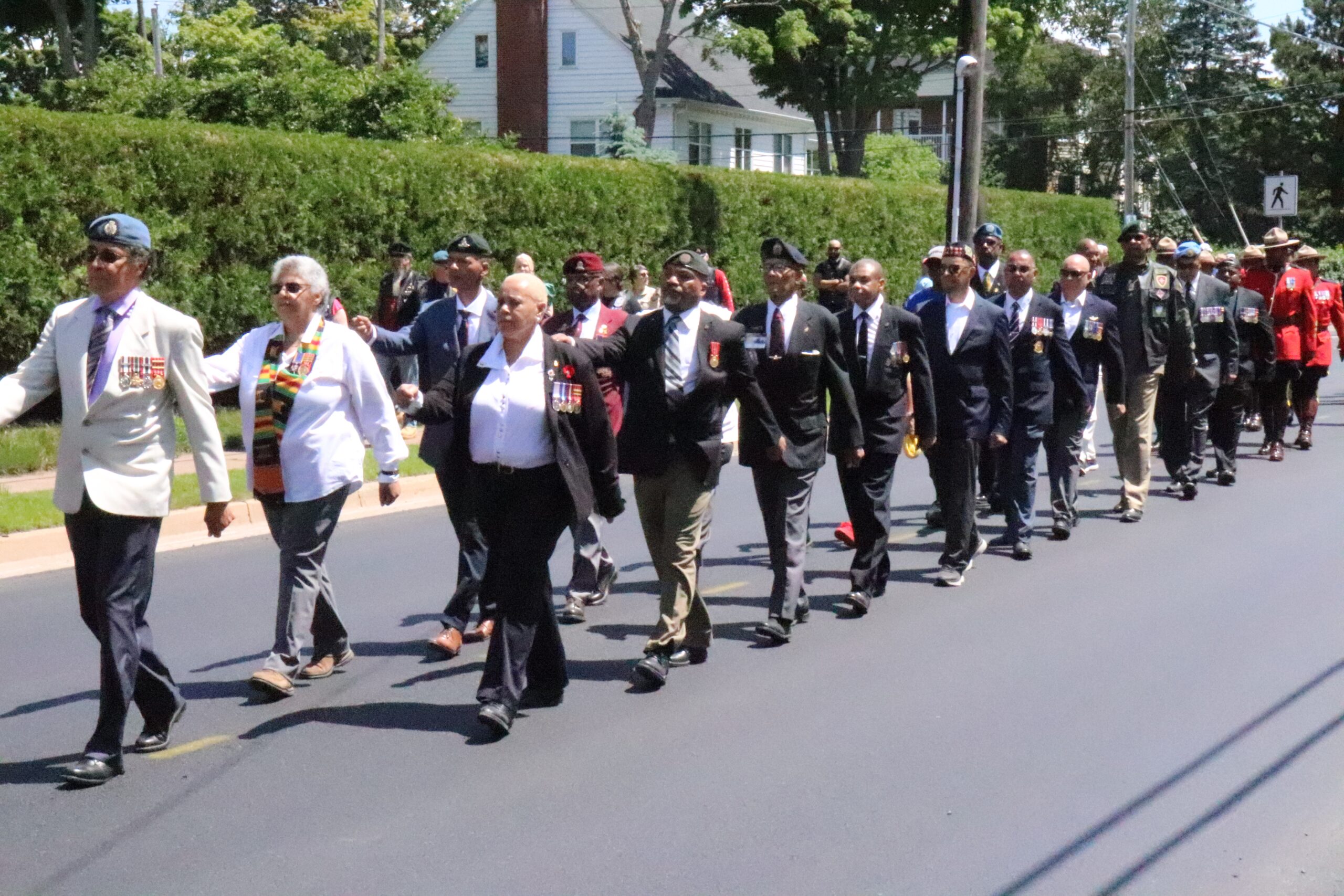 Servicepeople in different uniforms and wearing medals march down a street.