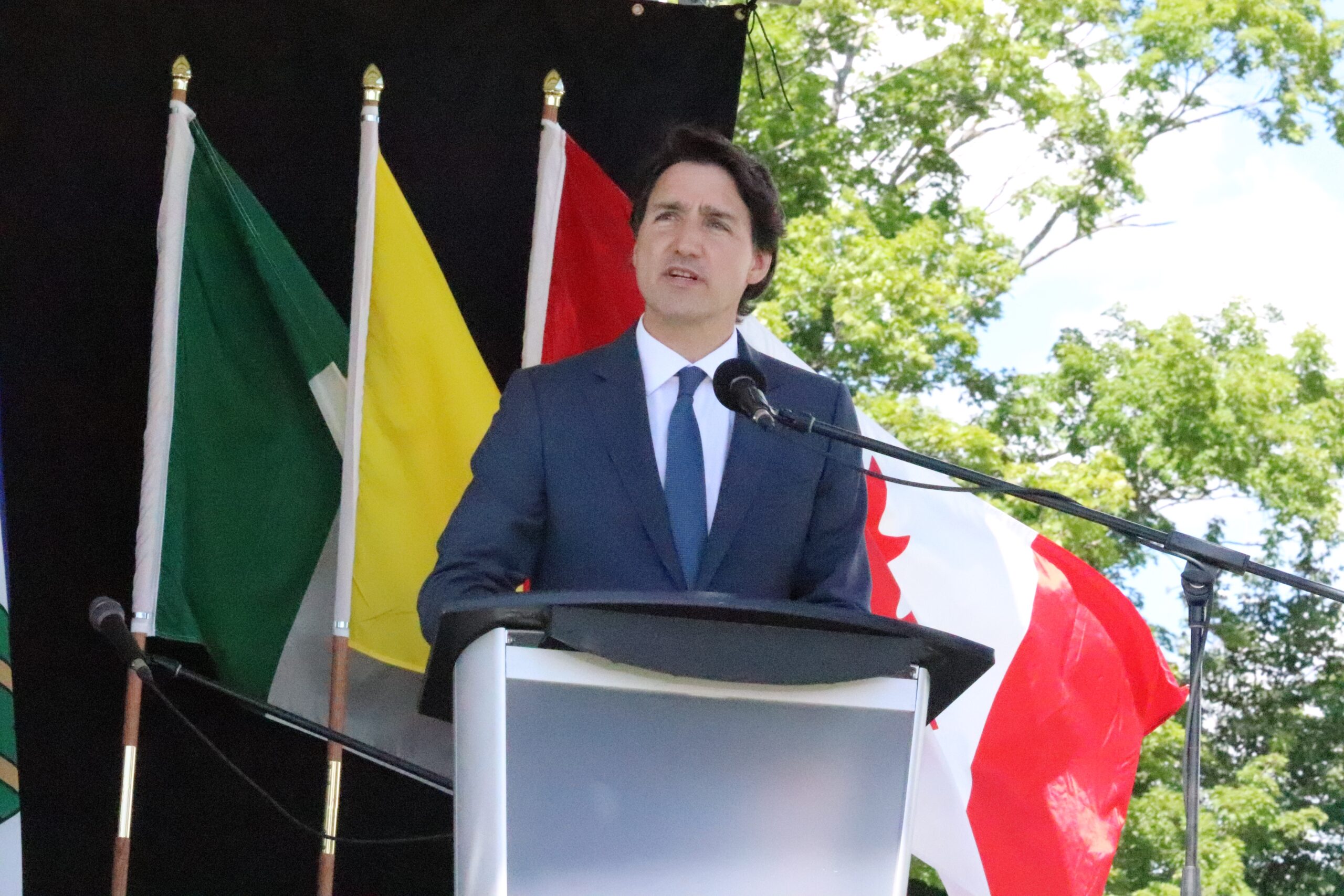 White man with dark hair and navy blue suit speaks at a microphone and podium.