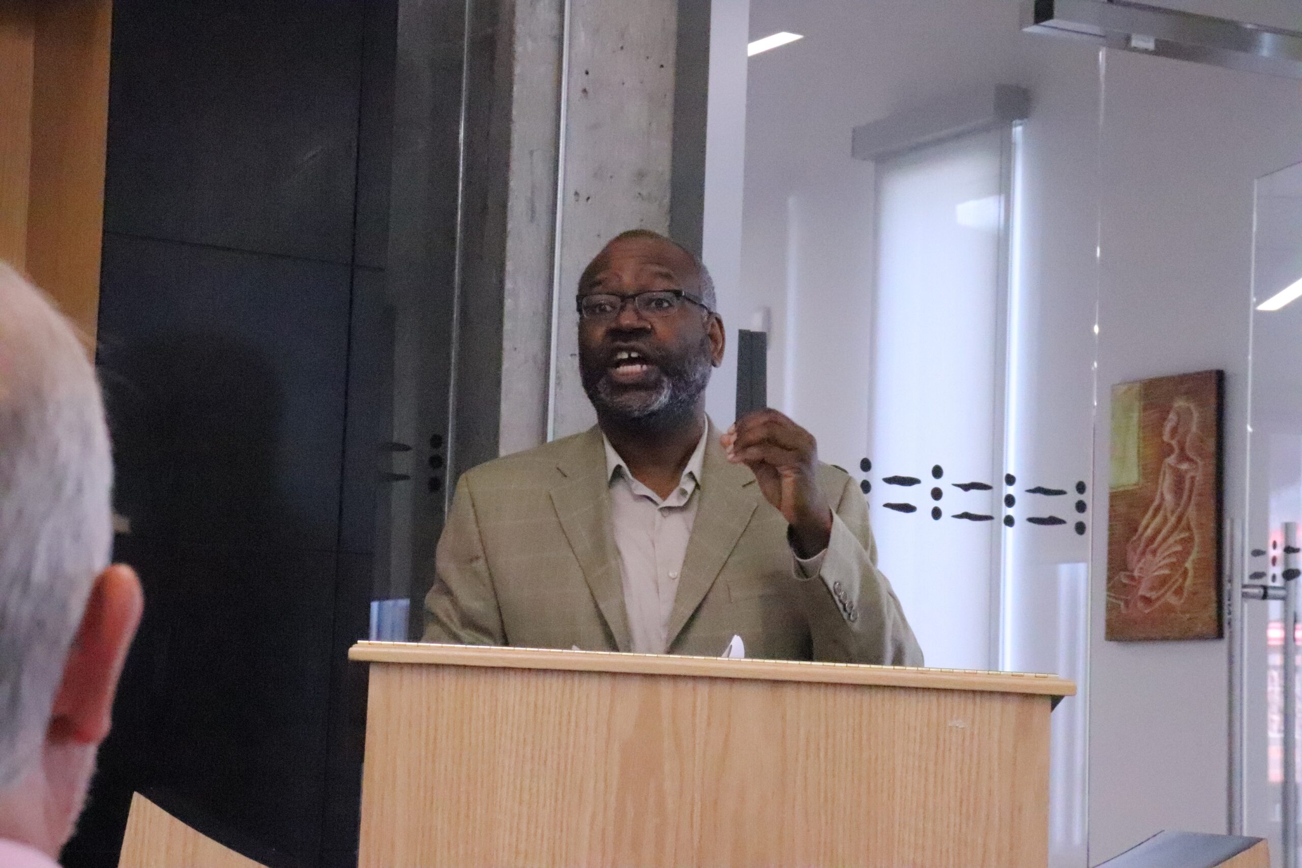 一个戴着眼镜和米色西装外套的黑人用讲台说话。