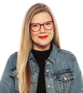 一个有着长长的金发的女人，戴着红色框架的眼镜，戴着红色唇膏，牛仔夹克和黑色上衣。