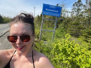 一位戴着墨镜的女士在路边自拍。一个社区的路边写着Mushaboom。