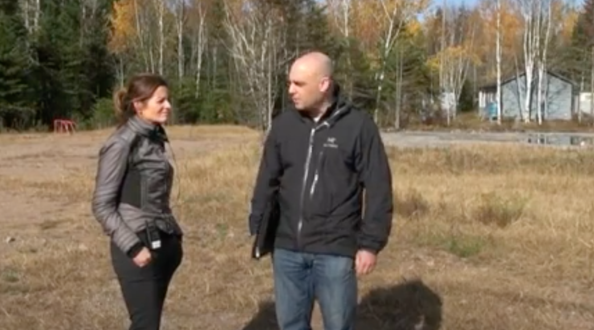 A woman and a man stand in an open field area.