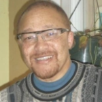 一个留着山羊胡、戴着酷酷的黑框眼镜的黑人对着镜头微笑。