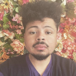 一个年轻的黑人男子，背景是花园里的粉红色花朵