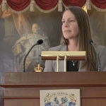 一位棕色头发的白人妇女站在讲台前，手里拿着麦克风