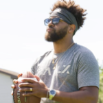 在一个阳光明媚的日子里，一个戴着太阳镜的黑人拿着足球