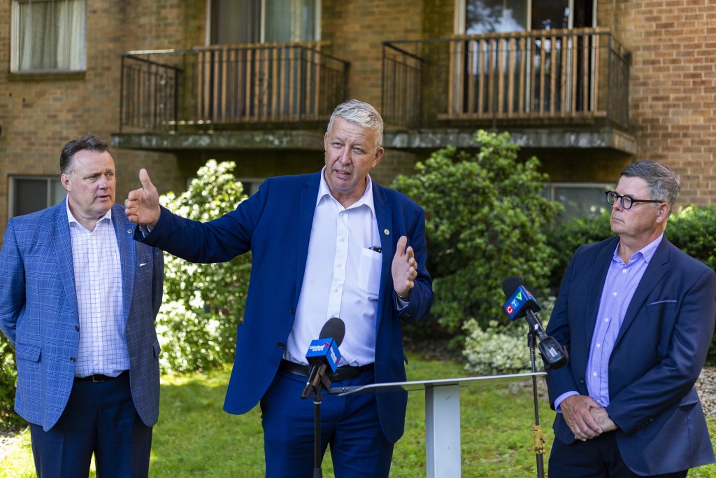 在一个阳光明媚的日子里，三个西装革履的男人站在一栋公寓楼外。