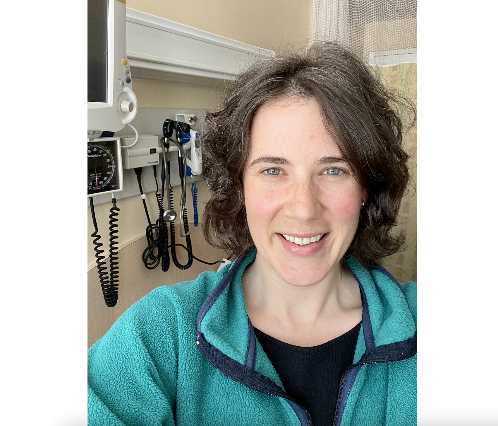 一位身穿黑色衬衫和鲜艳绿色毛衣的快乐微笑的妇女站在病房的医疗设备前。