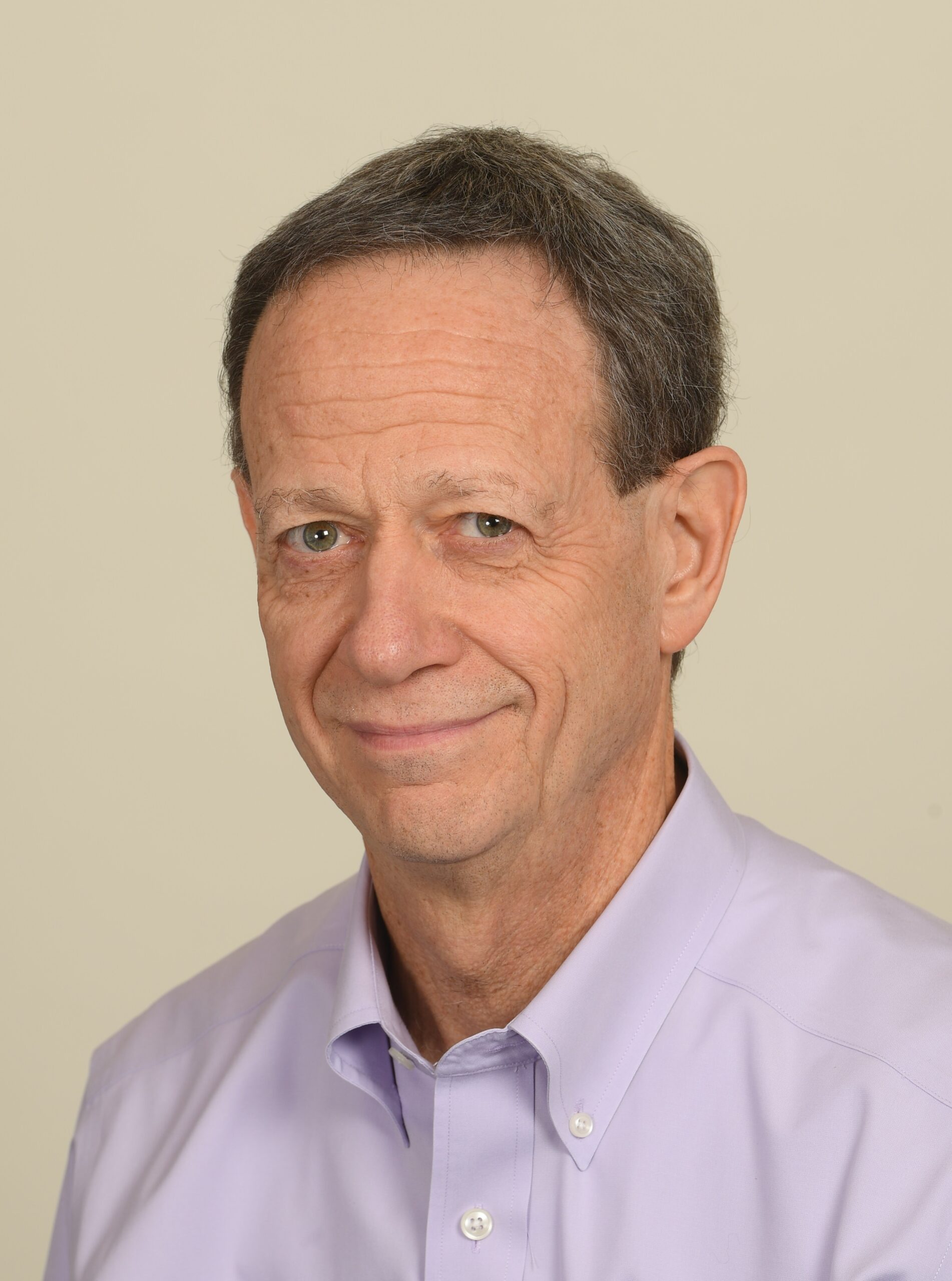 一名身穿淡紫色衬衫的男子微笑着看着米色墙壁上的摄像机。