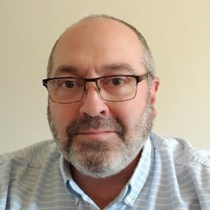 在奶油色的背景下，一个戴着眼镜、秃顶的白种人中年男子，留着胡子胡