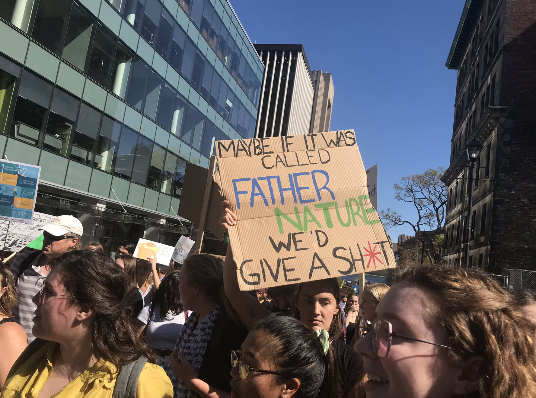 2019年9月27日，在哈利法克斯市中心的街道上，一名年轻女子在人群中站在蓝天下，举着一个牌子，上面写着“如果这被称为自然之父，也许我们会在乎”。