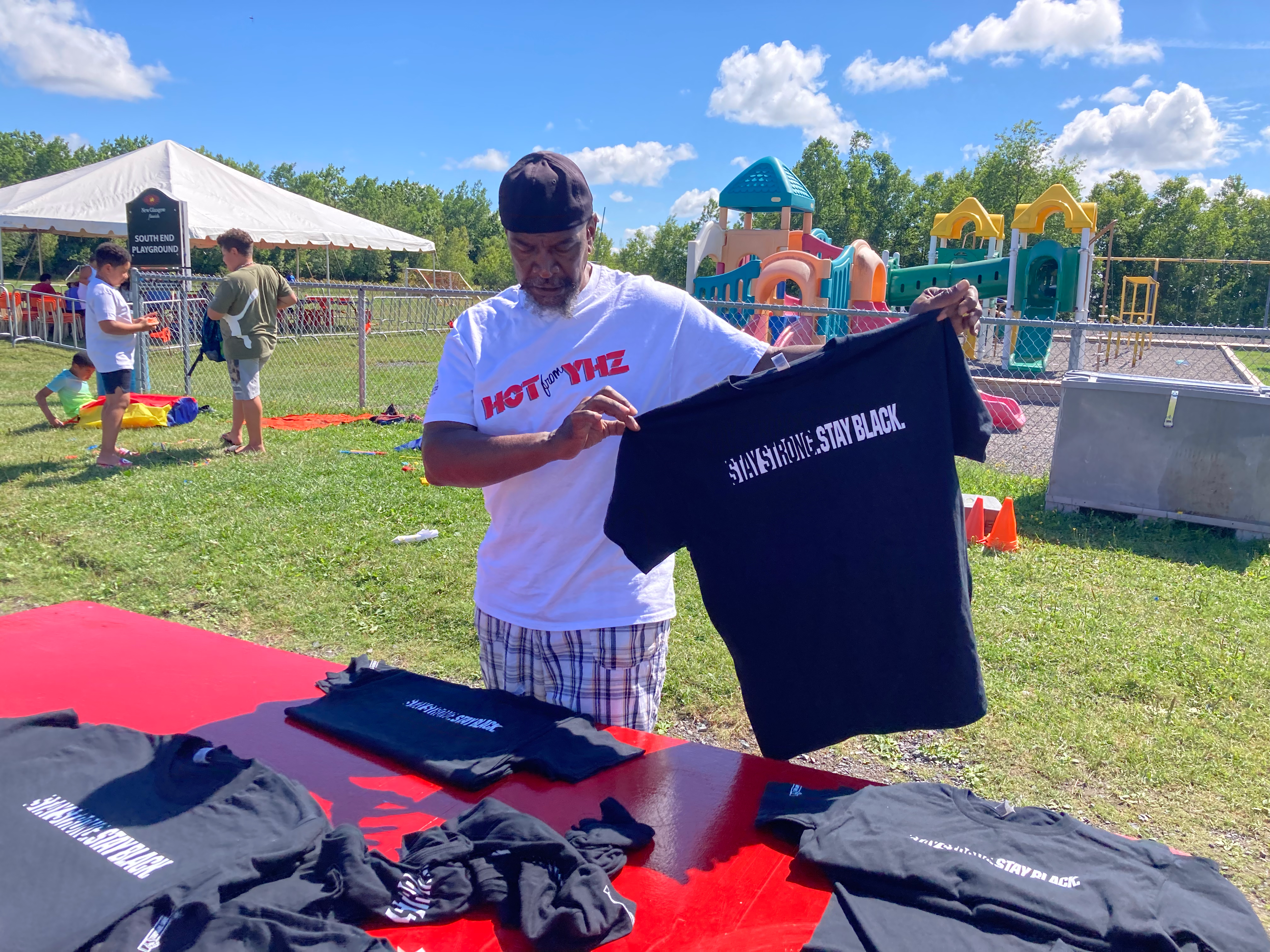 黑人男子在推销“坚强”。保持黑色。的t恤，背景是阳光和孩子们的游乐场