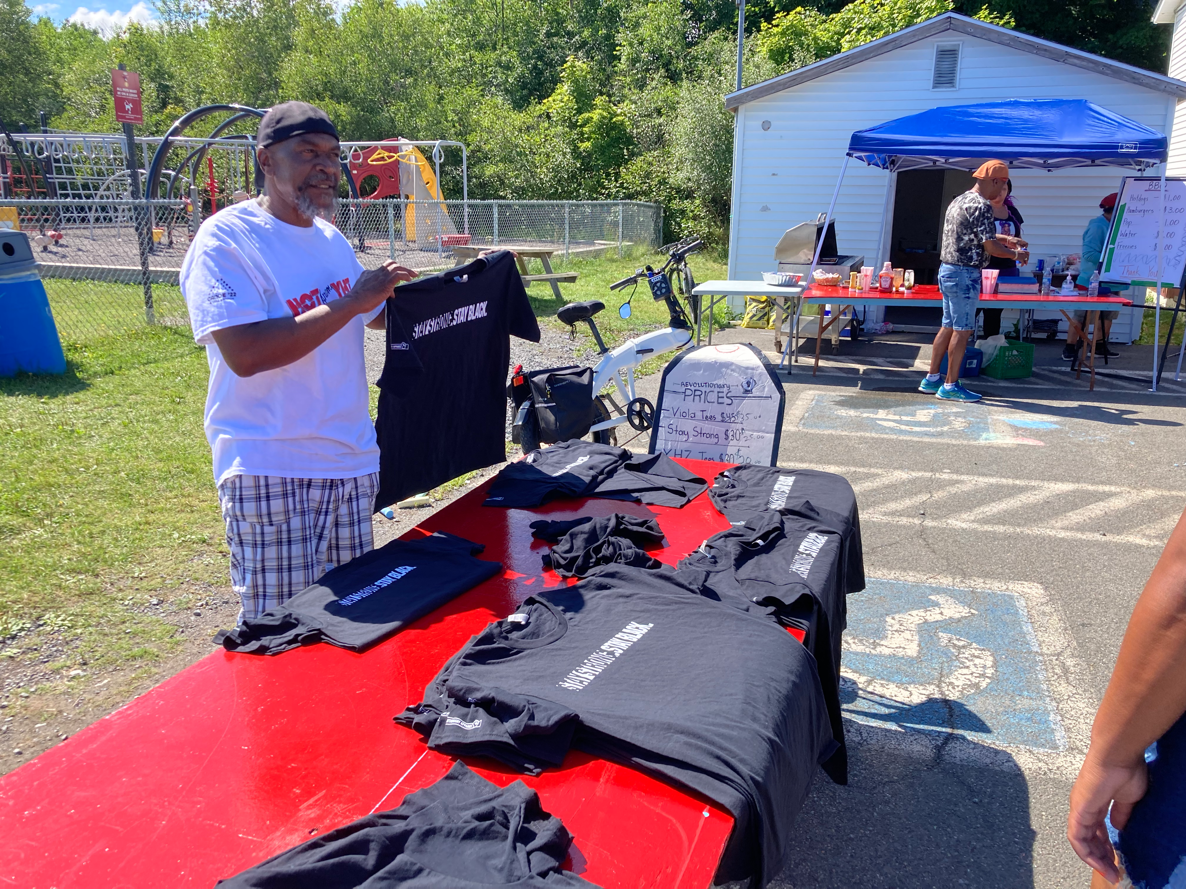 黑人男子在推销“坚强”。保持黑色。的t恤，背景是一个户外食堂