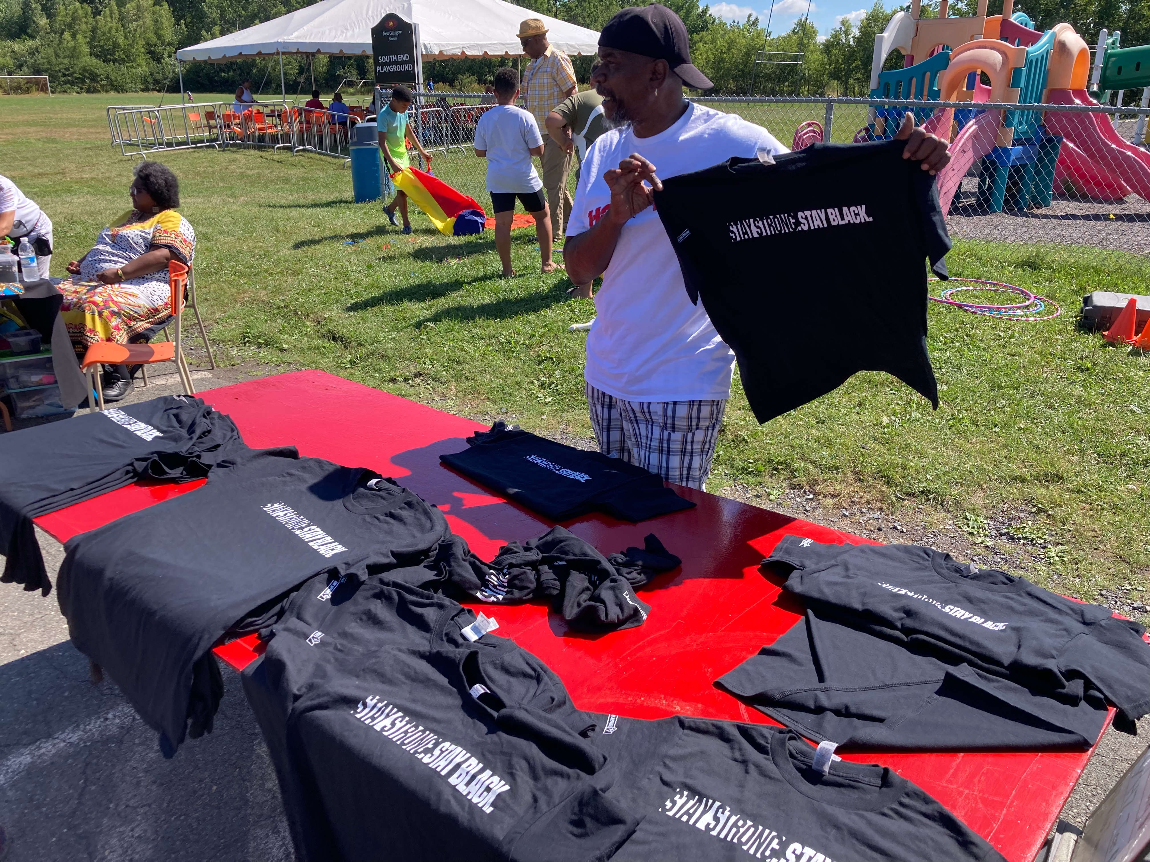 黑人男子在推销“坚强”。保持黑色。的t恤，背景是人们和一个操场