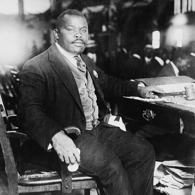 一张黑白照片，一个男人穿着西装坐在桌子上的椅子上。