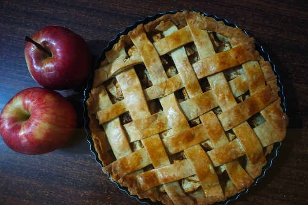 深色木桌上放着苹果派，旁边放着两个红苹果
