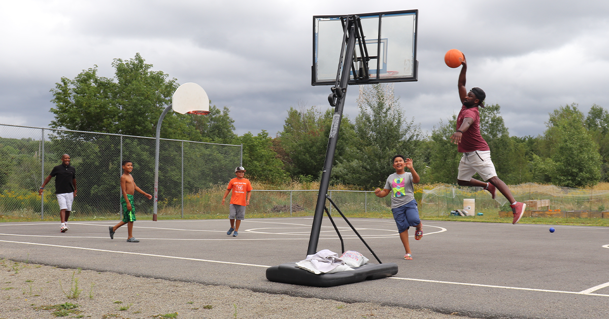 Black community members (three chidren and two men) play basketball on an outdoor basketball court during the 2022 New Glasgow Black Gala Homecoming