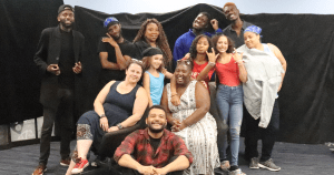 10名全黑人演员、白人舞台监督和黑人导演在黑色背景前摆姿势