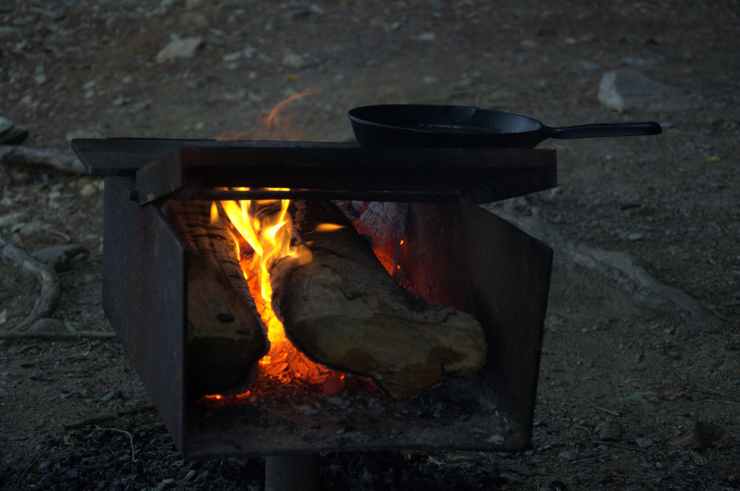 Fire burning in a metal fire box, with a cast iron pan on a grill above it.