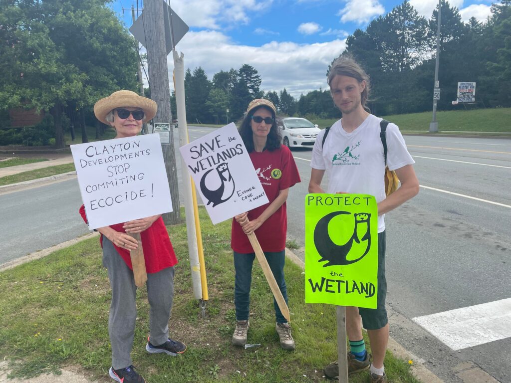 三名抗议者举着标语站在人行道上。