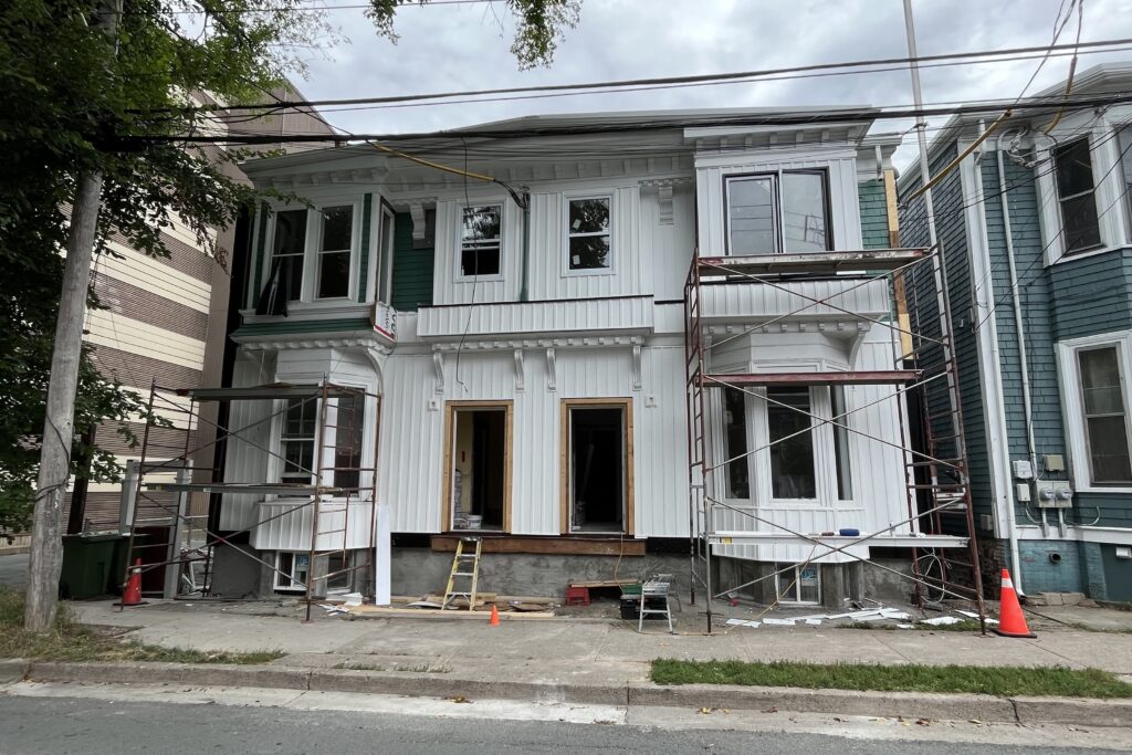 阴天，可以看到正在建设的对称的维多利亚式复式公寓。绿色的墙板被白色的木板和木条覆盖。