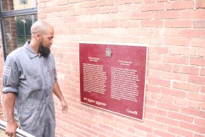 一名身穿灰色工作服的黑人男子在砖墙上安装了紫红色的Viola Desmond牌匾