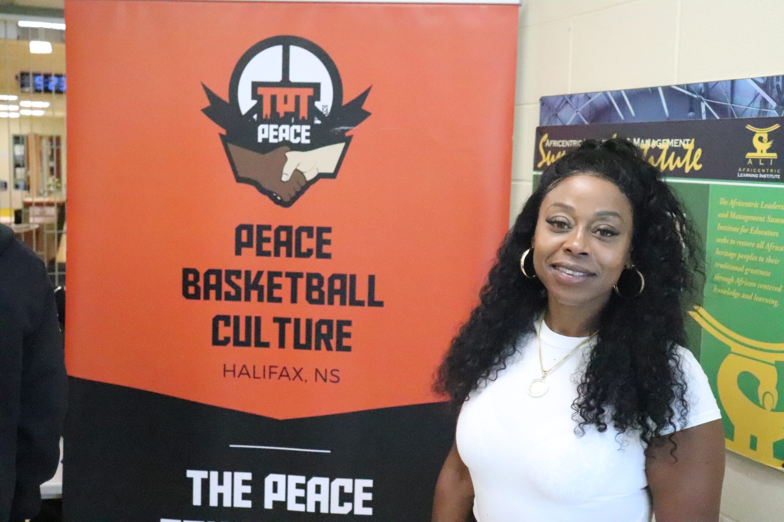 黑色长发、白色衬衫的黑人女子在“和平篮球文化”横幅旁微笑。