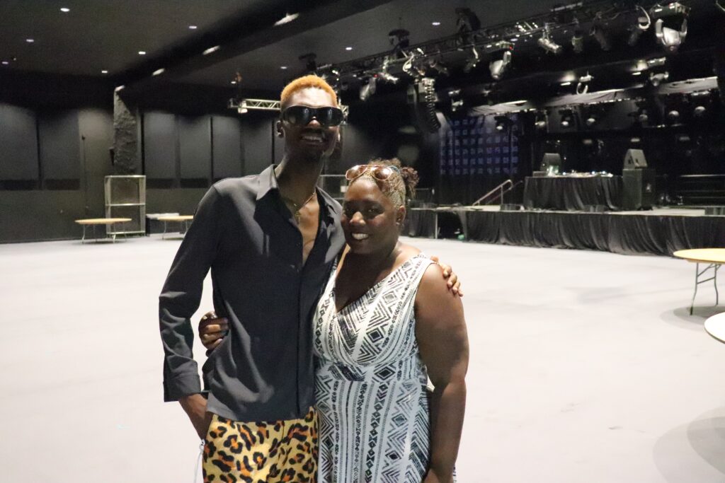 背景中，一名黑人男子和一名黑人女子在空无一人的剧院舞台前摆姿势。