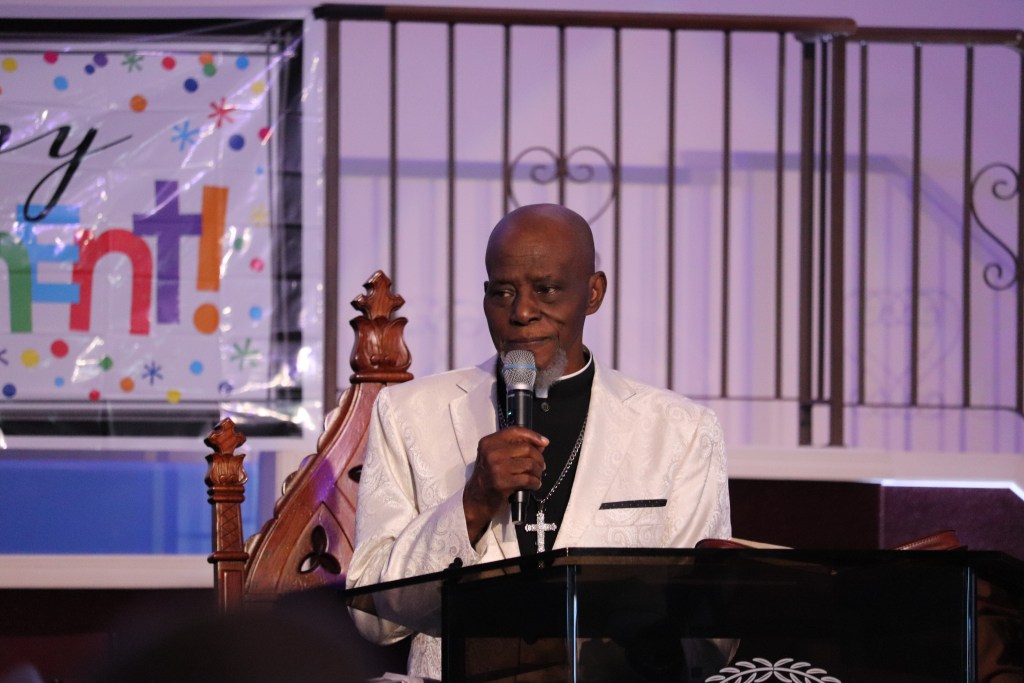 一名身穿白色西装的黑人男子在教堂讲台上布道