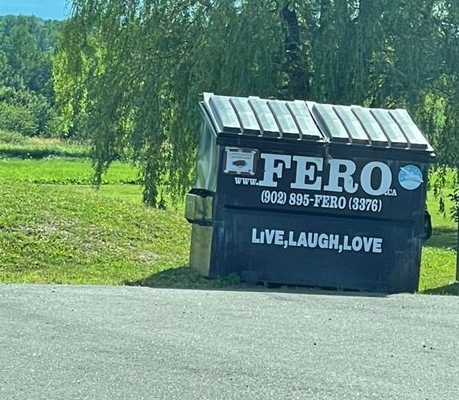 图为停车场里的深绿色垃圾桶，垃圾桶正面写着FERO公司的名字。垃圾箱上也贴着“活着，笑着，爱着”这句话。