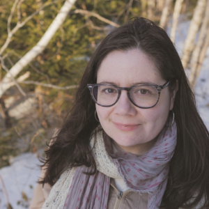 一个年轻的白种女人，一头长长的黑发，戴着眼镜，站在雪地里，背景是树