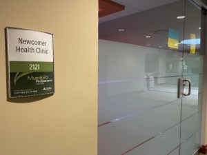 A sign on a wall outside a clinic with glass doors.