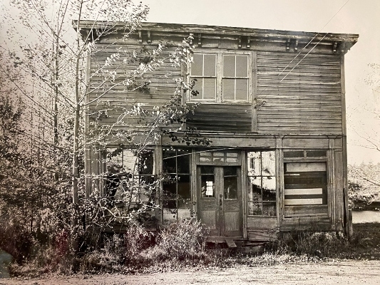 一张黑白照片，上面是一栋破旧的两层建筑，前面有一棵树