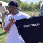 一个年轻的黑人男子在露天市场卖一件黑色T恤