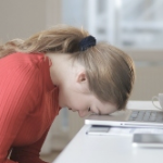 一个穿着红色毛衣的白人妇女把额头靠在打开的笔记本电脑上。