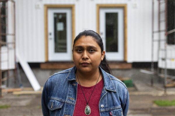 一名身穿红衬衫、牛仔夹克、戴着项链的女子站在一座在建建筑前。下雨了。