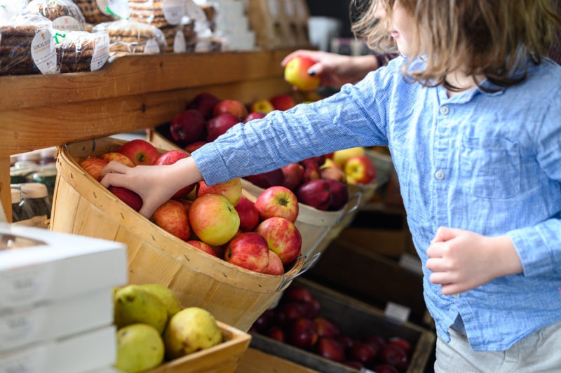 一个长头发的孩子把手伸进装满苹果的篮子里。