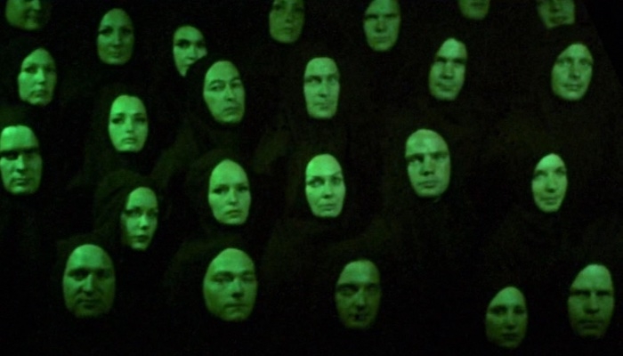 《星际迷航》(Star Trek)电视剧中的剧照，展示了一个人口过剩的世界，由于某种原因，一群人穿着黑衣，在绿光中行走，他们都面朝前方