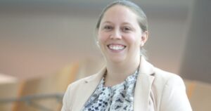 一个梳着马尾辫的微笑女人，身穿印有图案的上衣外搭奶油色西装外套。