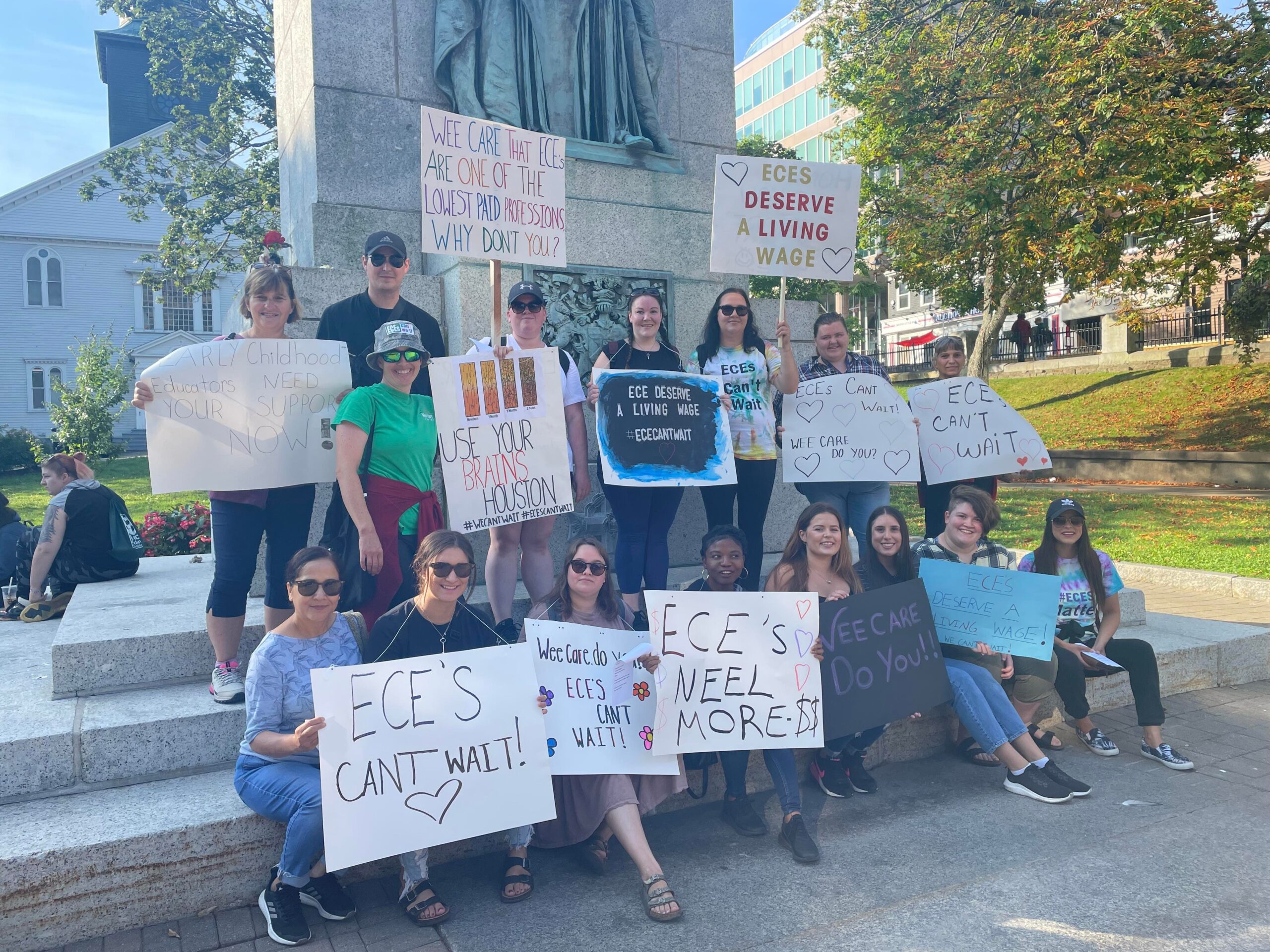 一群抗议者举着标语站在哈利法克斯市中心大游行的纪念碑前。