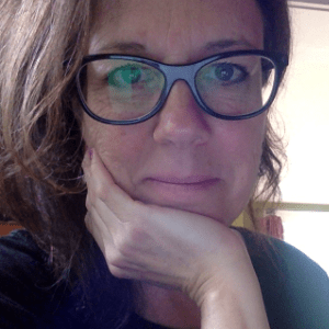 一个留着浅棕色卷发的白人妇女，穿着一件黑色上衣，戴着黑框眼镜，手托着脸躺在那里。