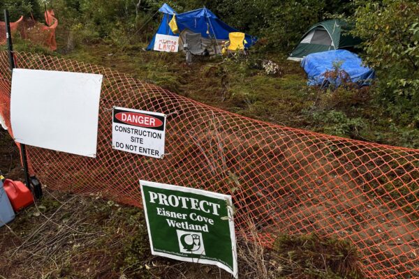 橙色的雪栅栏挡住了一片树林。篱笆后面是帐篷和椅子。这是一个阴天。
