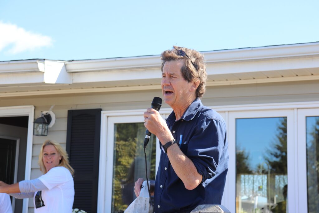 一名身穿蓝色衬衫的男子在一户人家前院举行的活动上通过麦克风讲话。