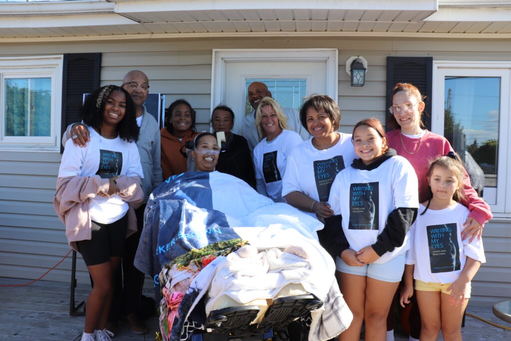 一名妇女坐在轮椅上，带着呼吸机，周围是她的直系亲属，他们对着镜头微笑