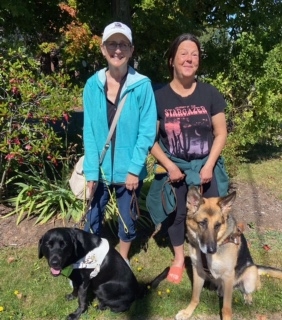 两个女人和她们的导盲犬站在公园里。