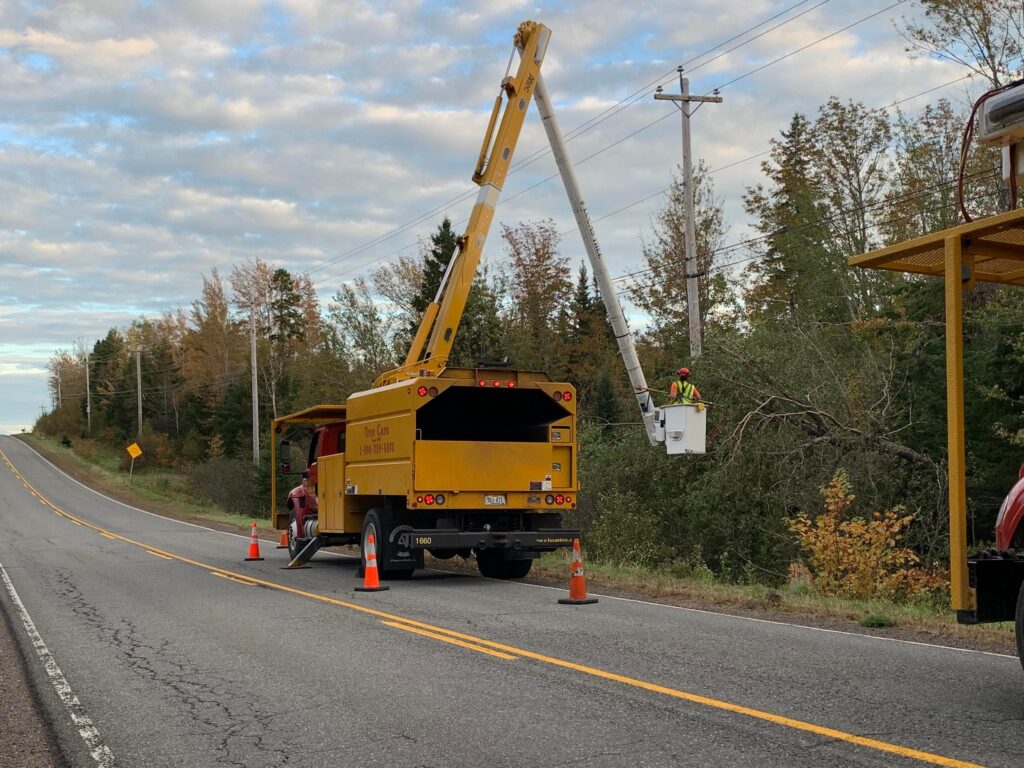 一名男子坐在一辆黄色多功能卡车的铲斗里，在乡村路边修理电线。