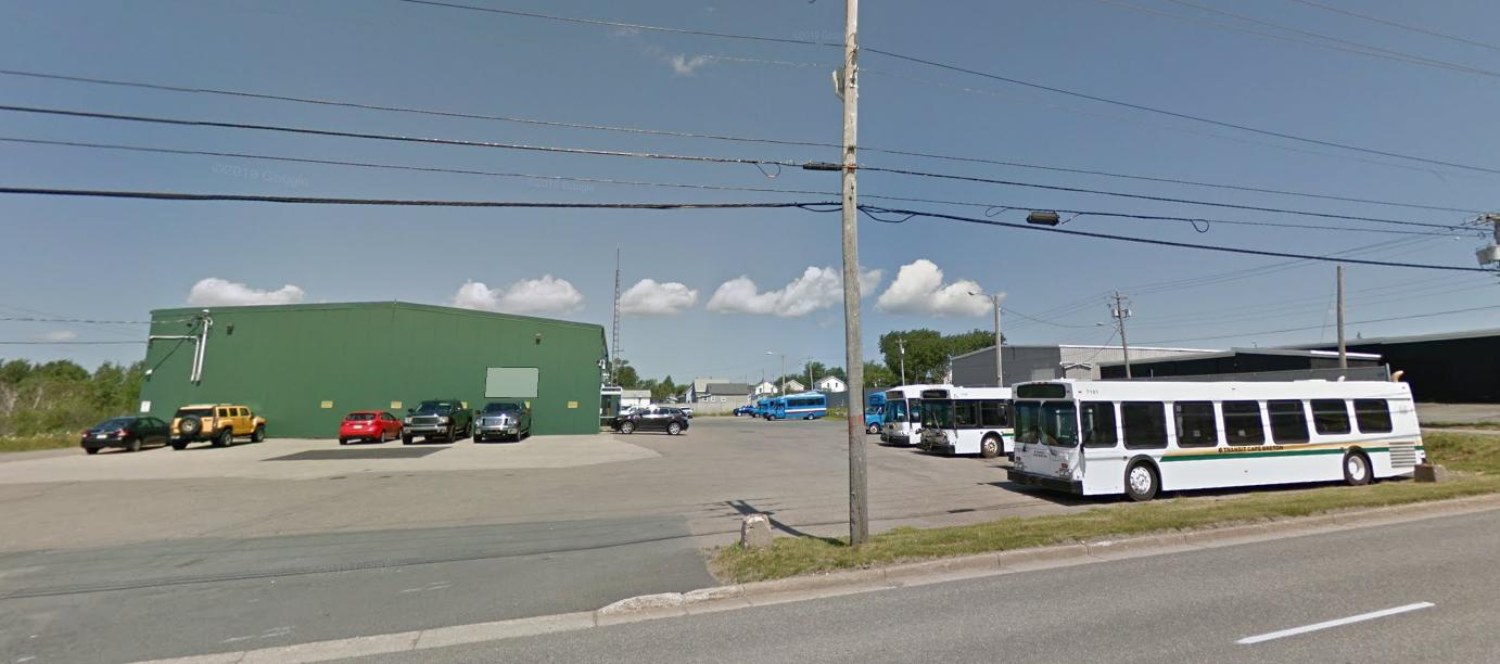 公共汽车停在仓库一样的绿色建筑旁的大停车场里